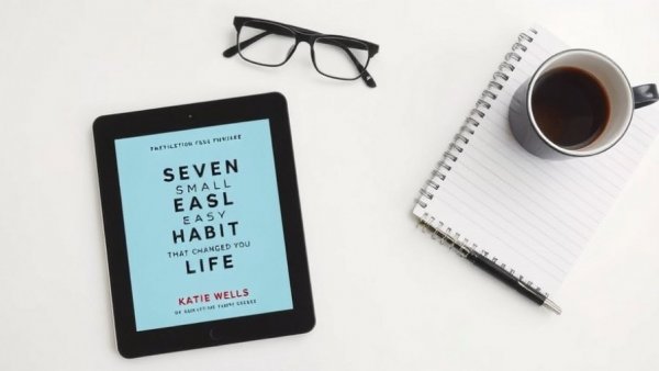 Flat lay tablet with book 'Seven Small Easy Habits' and coffee.