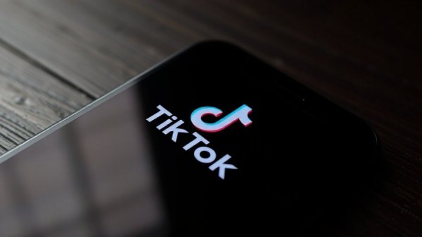 TikTok logo on smartphone screen, dark wooden table background.