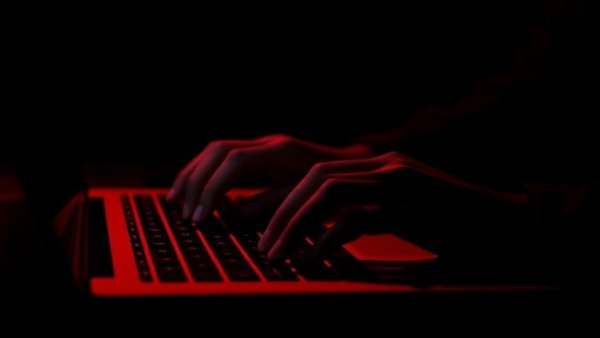 Shadowy hands typing on laptop keyboard, online child solicitation.