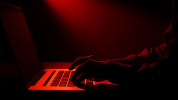 Silhouette hands on laptop in dim, warm-lit room.