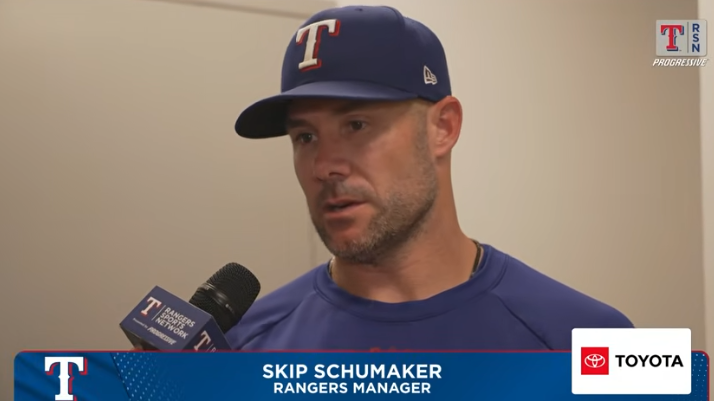 Blonde reporter interviews baseball manager indoors.