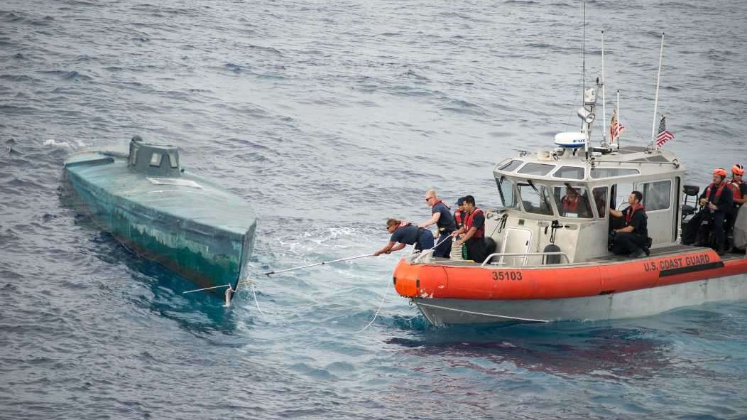 U.S. naval destroyer docked with bridge and cargo ship in background.