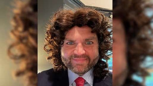 Man in a wig dressed in business attire, posing indoors with autumn decor, JD Vance Halloween meme.