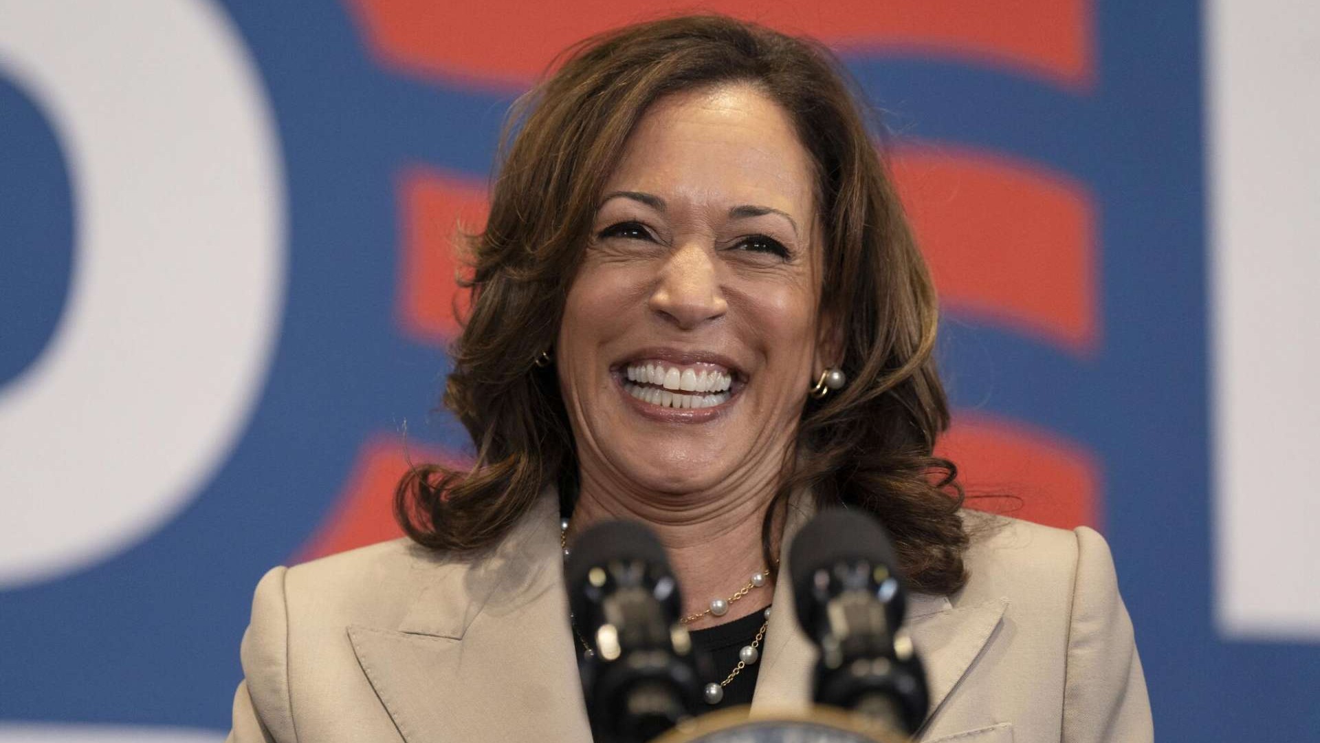 Breaking news: woman speaks at event with American flag backdrop.