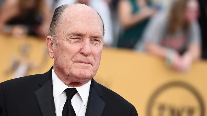 Distinguished man smiles while holding an award.