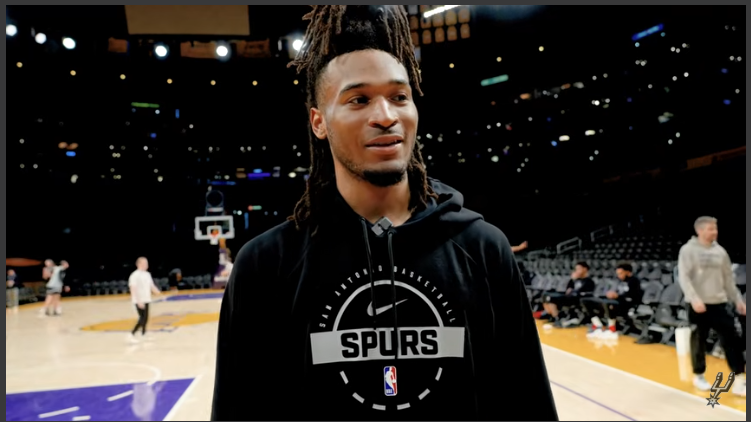 NBA playoffs player with dreadlocks in San Antonio jersey pointing on the court.
