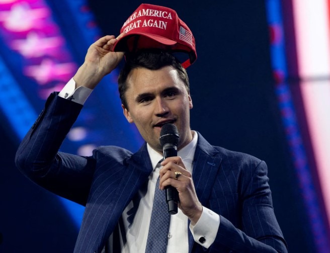 Smiling man in a blazer at a vibrant indoor event with a crowd.