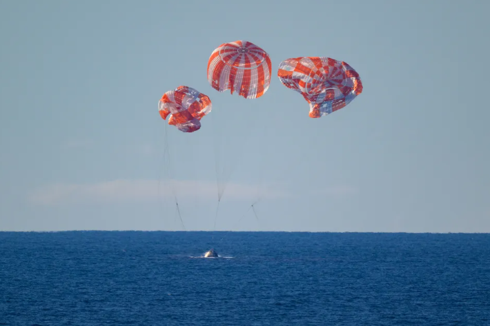 NASA astronauts' capsule from the Artemis program descends with vibrant red parachutes into the ocean.