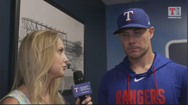 Interviewer speaks with man in baseball cap during postgame interview.