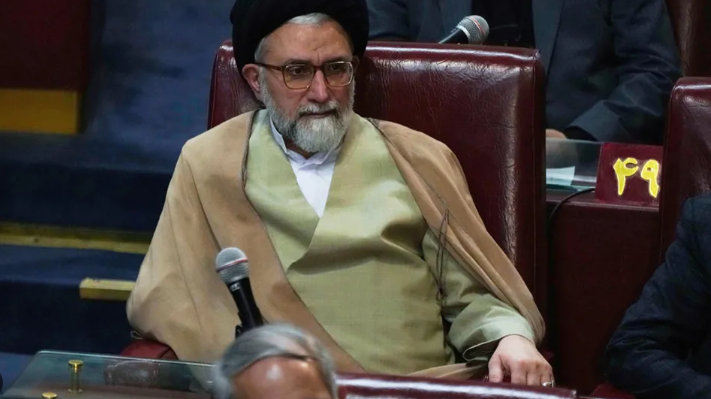 Iran intelligence chief impact on US, serious older man by Iranian flag.