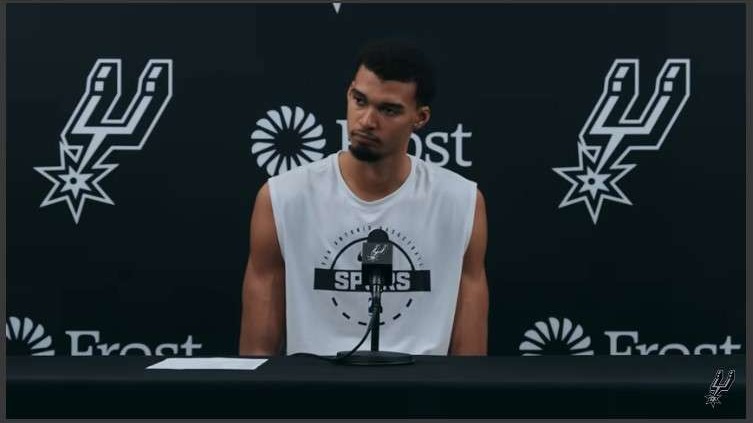 San Antonio Spurs player speaking at a press conference, focused expression.