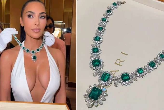 Elegant woman with emerald necklace posing in luxurious hallway.